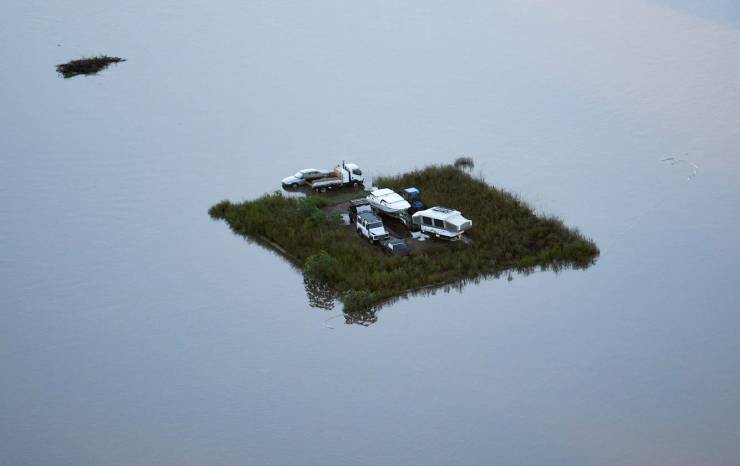Several cars and boats parked on the flooded piece of land.