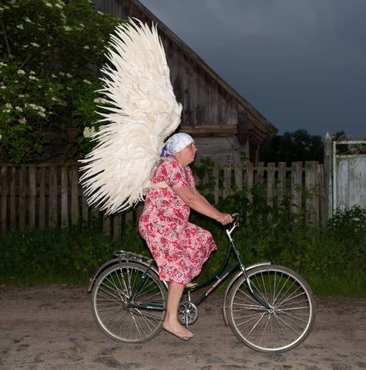 Grandmother with angel wings is riding on a bicycle.