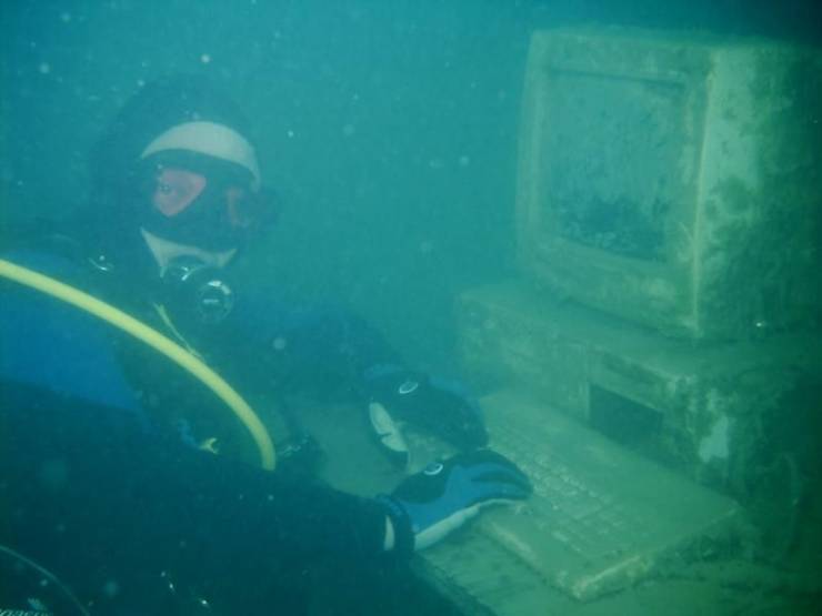 A scuba diver pretending to work at ancient Pentium PC underwater.