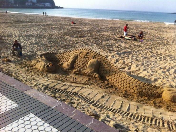 An amazing sand sculpture of a dragon on a beach.
