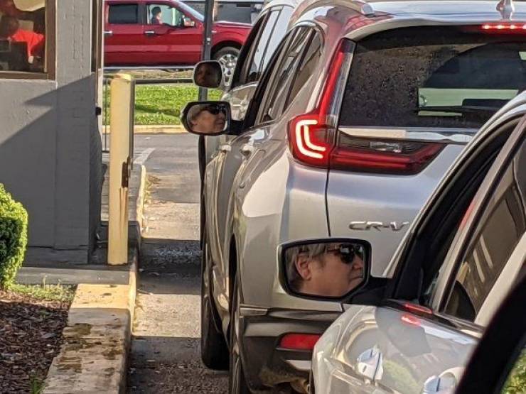 Cars with similar-looking drivers reflecting in the car mirrors wait in line.