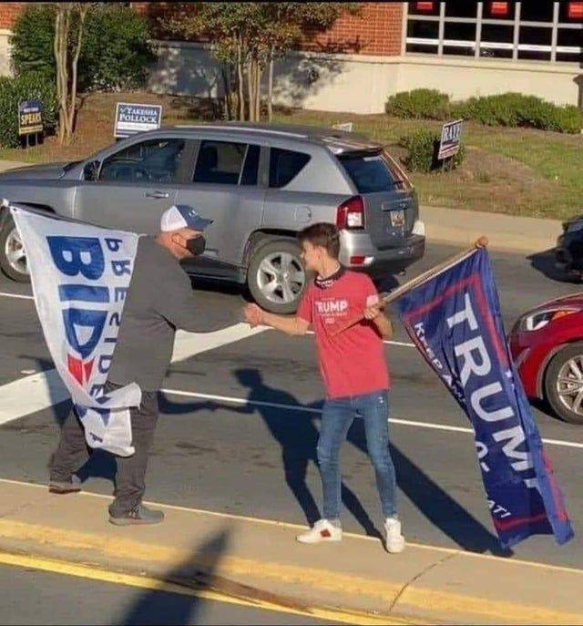 Two protesters carrying "Biden" and "Trump" flags shake hands.