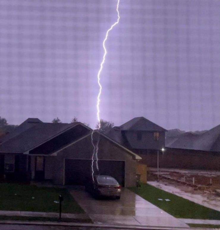 A flash of huge lightning strikes a car parked by a garage.