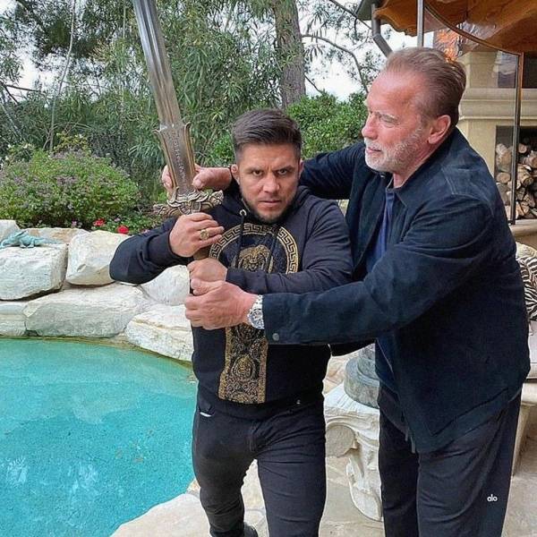 Arnold Schwarzenegger shows a man how to hold a sword.