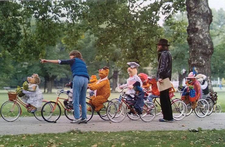 A woman shows the way to children riding bicycles and dressed in Muppet Show characters.
