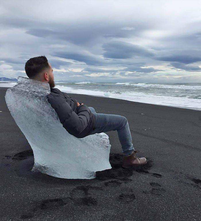 A man sitting on an ice chair at the beach with black sand.