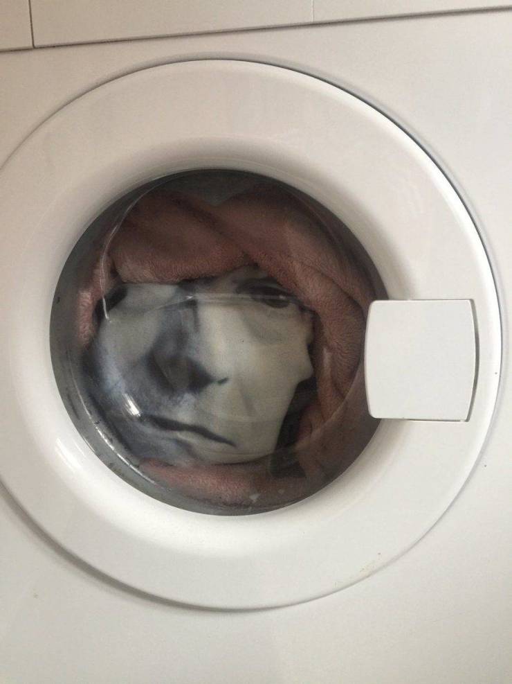 A window of a washing machine with a persons face peeping from it.